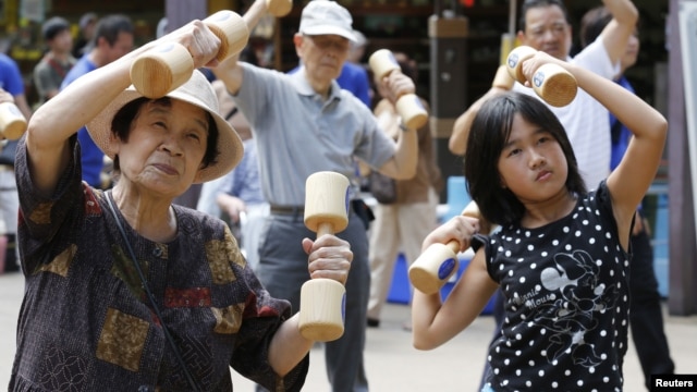 A girl exercises with other people using wooden dumbbells during a health promotion event to mark Japan's "Respect for the Aged Day" at a temple in Tokyo on September 17, 2012.
