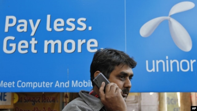 A man speaks on a mobile phone in front of a billboard of Uninor at a market in Ahmedabad, February 6, 2012.  Telenor's joint venture with Unitech, which operates under the Uninor brand, has been among the most aggressive of India's newer telecoms compani