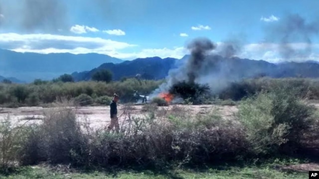 A man stands near the smoking remains of a helicopter that crashed with another near Villa Castelli in the La Rioja province of Argentina, Monday, March 9, 2015.