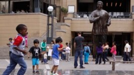 Children play beneath a giant statue of former South African President Nelson Mandela, center back, on Nelson Mandela Square in Sandton, Johannesburg, Sunday, Mar. 10, 2013.