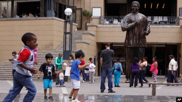 Children play beneath a giant statue of former South African President Nelson Mandela, center back, on Nelson Mandela Square in Sandton, Johannesburg, Sunday, Mar. 10, 2013.