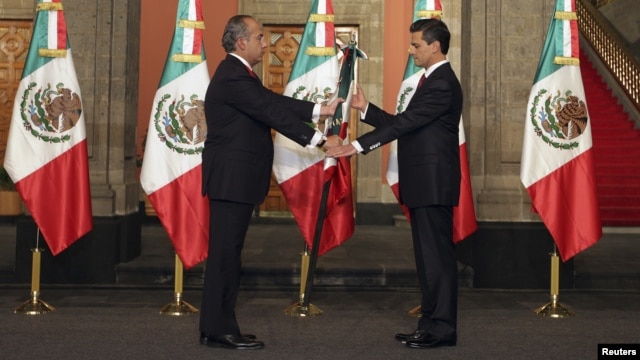 Outgoing leader Felipe Calderon (L) hands the national flag to Mexico's new president, Enrique Pena Nieto, during a midnight ceremony at the National Palace in Mexico City, Dec. 1, 2012. 