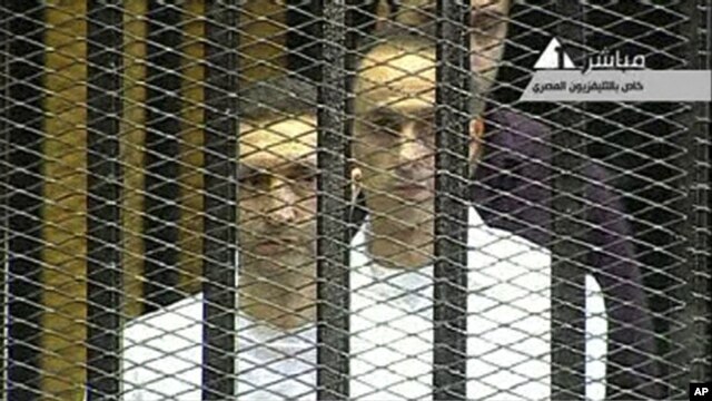 This video image taken from Egyptian State Television shows the sons of  Hosni Mubarak, Alaa Mubarak, left and Gamal Mubarak as they  stand inside the  cage of mesh and iron bars in a Cairo courtroom Wednesday Aug. 3, 2011 as his historic trial began on c