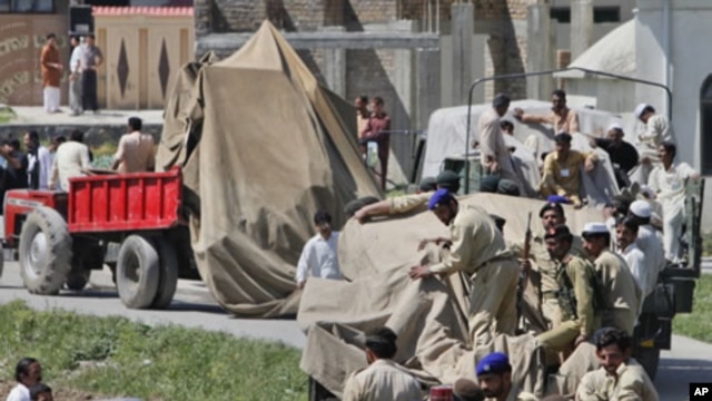 Soldiers and residents stand over covered debris, as it was moved out by military vehicles from the compound within which al-Qaida leader Osama bin Laden was killed, in Abbotabad, May 2, 2011