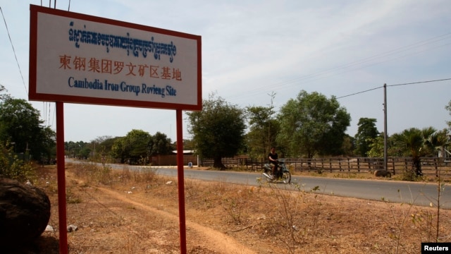 A man rides a motorcycle past a signboard for the Cambodia Iron Group at the Rovieng District in Preah Vihear province, February 10, 2013.