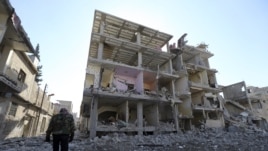 Wani mayakin 'yan tawaye akan hanyarshi a gaban wani gini da sojojin gwamnati suka fasa a unguwar Mleha dake birnin Damascus Junairu 21, 2013.