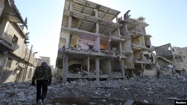 A fighter of Free Syrian Army's Tahrir al Sham brigade walks in front of building destroyed during yesterdays Syrian Air force air strike in Mleha suburb of Damascus January 21, 2013.