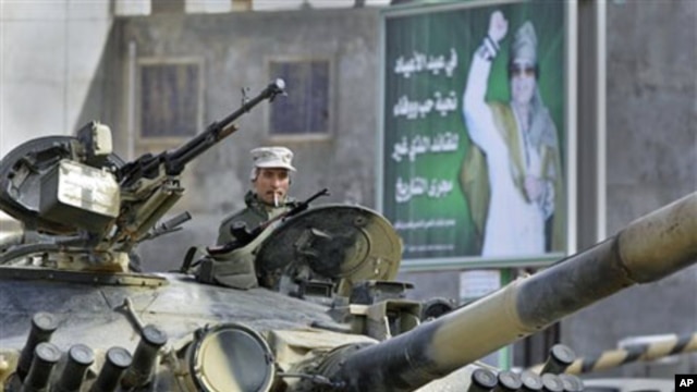 A Libyan army soldier loyal to Libyan leader Moammar Gadhafi, on poster in background, sits in a tank, in Qasr Banashir, southeast of the capital Tripoli, March 1, 2011
