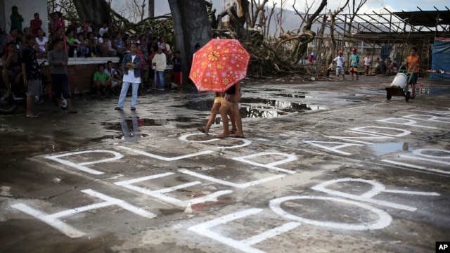 Survivors of Typhoon Haiyan walk over a "Help" message painted on a concrete floor, Saturday, Nov. 16, 2013 in Burauen town, Leyte province, central Philippines.