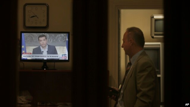 Greek Prime Minister Alexis Tsipras is seen on a screen during a televised address to the nation, as a staffer of the Greek Presidential Palace looks on, in Athens, Aug. 20, 2015.