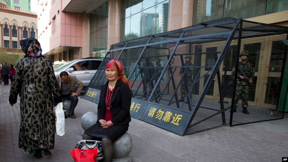 2014年5月1日,一位维吾尔妇女坐在乌鲁木齐街头,身后是铁笼保护下的中国武警。