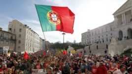 Demonstrators wave a Portuguese flag and shout slogans outside the parliament, at right, during a workers protest, Lisbon, Thursday, March 22, 2012.
