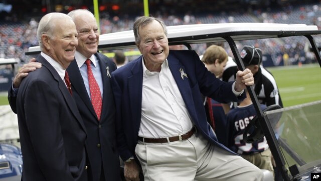 Former President George H. W. Bush, right, former Secretary of State James Baker, left, and Houston Texans owner Bob McNair pose together before an NFL football game against the Buffalo Bills in Houston, November 4, 2012.