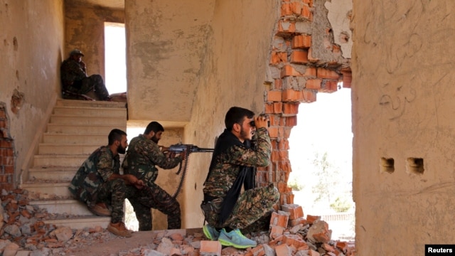 FILE - Kurdish People's Protection Units (YPG) fighters take up positions inside a damaged building in al-Vilat al-Homor neighborhood in Hasaka city, Syria, as they monitor local movements of Islamic State fighters.