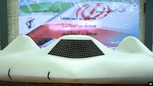 This photo released on Thursday, Dec. 8, 2011, by the Iranian Revolutionary Guards and taken at an undisclosed location claims to show the US RQ-170 Sentinel drone which Tehran says its forces downed earlier this week. In the banner in background depictin