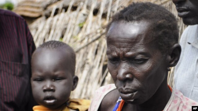 In this photo of Thursday, Jan.12, 2012 a mother waits with her son for emergency food rations from the World Food Program in the town of Gumuruk, 35 kilometers southwest of Pibor, South Sudan. Tens of thousands fled their homes after ethnic violence erup