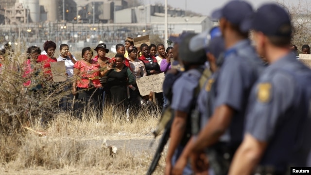 Police look on as women carry placards in protest against the killing of miners by the South African police on Thursday, outside a South African mine in Rustenburg, 100 kilometers northwest of Johannesburg, August 17, 2012.