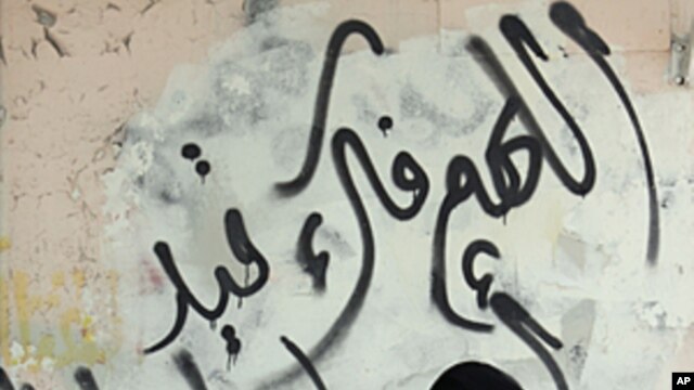 A Bahraini woman shops for produce on Tuesday, October 4, 2011, in the Shi'ite Muslim village of Malkiya, Bahrain. The graffiti on the wall behind her reads: "God, free our prisoners."