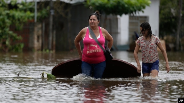 A woman (L) and her daughter carry a table on a flooded street as they leave their home in San Miguel neighborhood in Asuncion, Paraguay. Dec. 27, 2015.