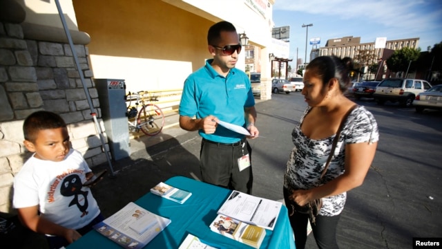 FILE - Jaime Corona, patient care coordinator at AltaMed, speaks to a woman during a community outreach on Obamacare in Los Angeles, California.