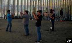 Personas graban con sus teléfonos el muro que separa Tijuana, México de Estados Unidos, el jueves 10 de enero de 2019.