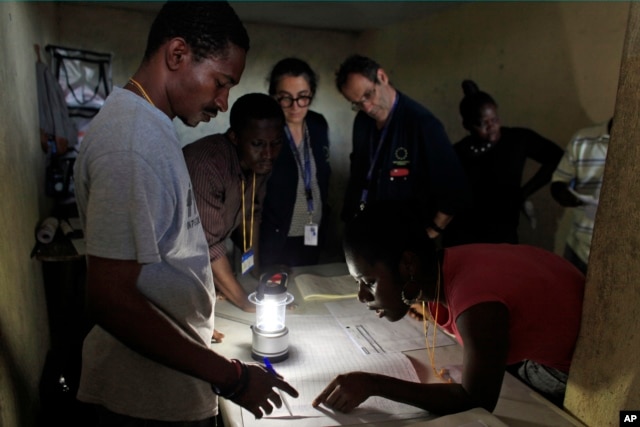 Members of the European Union Election Observation Mission, behind, observe electoral workers count ballots at a polling station at the end of the national elections in Port-au-Prince, Haiti, Oct. 25, 2015.