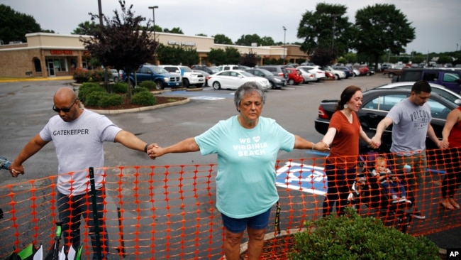 Lisa Dunaway (centro), residente de Virginia Beach, Virginia, se da la mano con recolectores de basura de la ciudad durante una vigilia en respuesta a un tiroteo en un edificio municipal. 1 de junio de 2019.