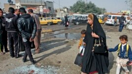 A woman with her children walks past at the site of a suicide bombing attack in the Shi'ite neighborhood of Kadhimiya in Baghdad, Iraq, Feb. 9, 2015.