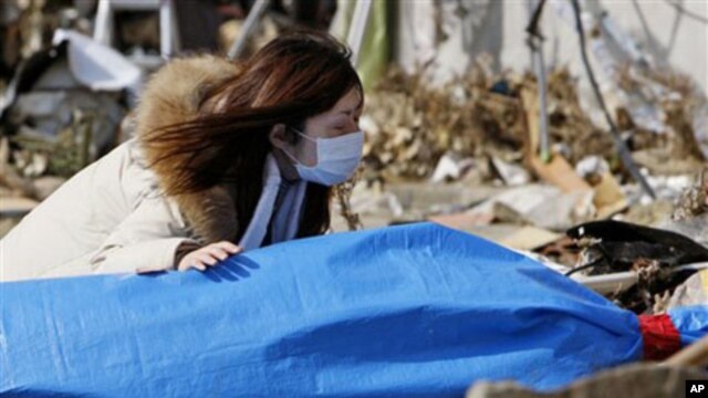 Tayo Kitamura, 40, kneels in the street to caress and talk to the wrapped body of her mother Kuniko Kitamura, 69, after Japanese firemen discovered the dead woman inside the ruins of her home in Onagawa,  March 19, 2011