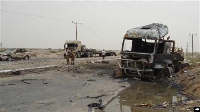 Soldiers stand by a burned out military vehicle at the site of an attack in Aden, Yemen, July 24, 2011. A suicide attacker driving a pickup truck packed with explosives blew himself up outside an army camp in Yemen's coastal city of Aden, killing at least