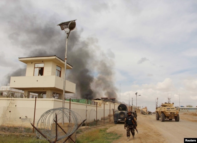 A member of the Afghan security forces walks as smoke billows from a building after a Taliban attack in Gereshk district of Helmand province, Afghanistan, March 9, 2016.