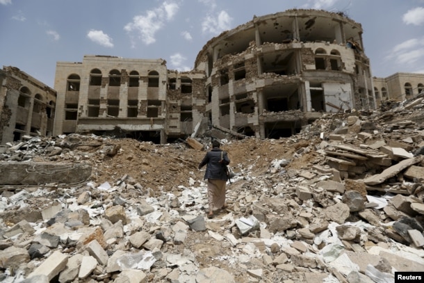 FILE - An Iranian-allied Houthi militant walks in front of a government compound, destroyed by recent Saudi-led airstrikes, in Yemen's northwestern city of Amran, July 27, 2015.
