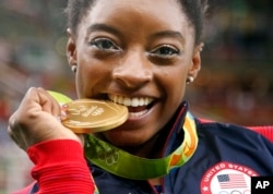 Vận động viên thể dục dụng cụ của Mỹ Simone Biles cắn chiếc huy chương vàng mà cô giành được trong phần thi toàn năng nữ ở Thế vận hội Mùa hè Rio de Janeiro, Brazil, ngày 11 tháng 8 năm 2016.