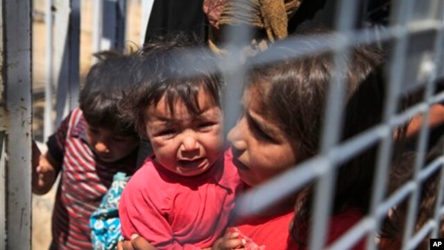 A Syrian child carries a baby crying while they wait with others to cross back to the border town of Tal Abyad in Syria from Turkey, at the border crossing in Akcakale, southeastern Turkey, June 17, 2015.
