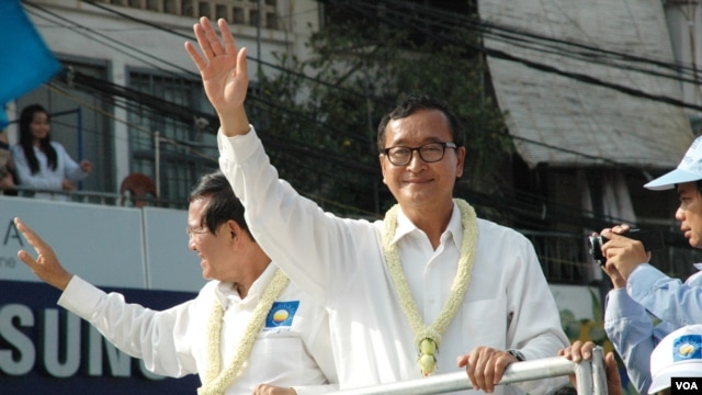 FILE - Opposition leader Sam Rainsy (white shirt, right), and deputy opposition leader Kem Sokha (left) wave to people watching the march, Phnom Penh, Cambodia. (Robert Carmichael/VOA).