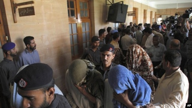 Pakistani police officers escort security officials with their faces covered, who were allegedly involved in the killing of a boy, to a police van at a local court in Karachi, June 13, 2011.