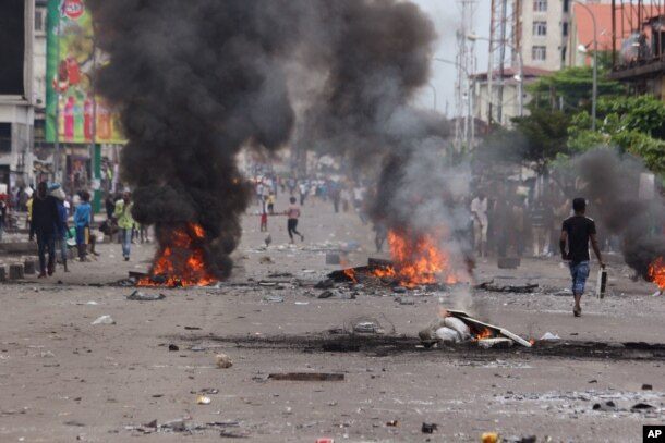 People walk near burning debris during election protests in Kinshasa, Democratic Republic of Congo, Monday, Sept. 19, 2016.