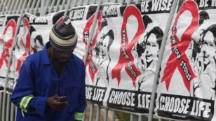 FILE - A man talks on a mobile phone as he walks past World AIDS Day banners in Johannesburg, South Africa, Dec. 1, 2014.