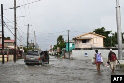 A vehicle and pedestrians make their way through a street flooded by heavy rain before the arrival of Hurricane Lisa in Belize City on Nov. 2, 2022.