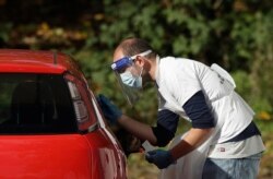 A person is tested for COVID-19 at a drive-through testing center in a car park in Chessington, Greater London, Oct. 7, 2020.