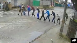 In this image from March 4, 2022, surveillance video provided by the Ukrainian government, Russian troops lead nine men at gunpoint to their headquarters on Yablunska Street in Bucha, where they would be tortured and executed. The men were picked up as part of what Russian soldiers called “zachistka” – cleansing.