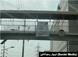 شعارنویسی بر روی پارچه آویزان شده از یک پل عابر پیاده در اهواز