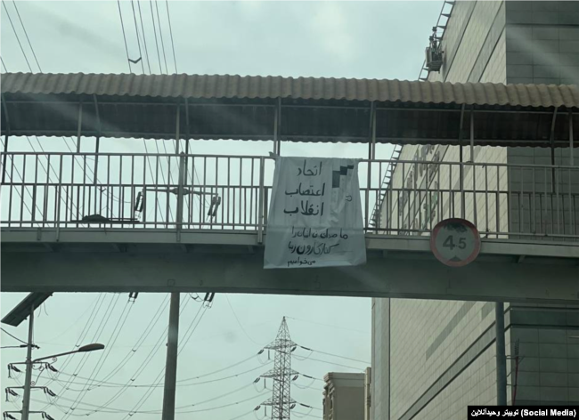 شعارنویسی بر روی پارچه آویزان شده از یک پل عابر پیاده در اهواز