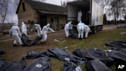 FILE: FILE - Volunteers load bodies of civilians killed in Bucha onto a truck to be taken to a morgue for investigation, in the outskirts of Kyiv, Ukraine, Tuesday, April 12, 2022. Russian soldiers called their sweeps of Bucha and other towns “zachistka” – cleansing. 