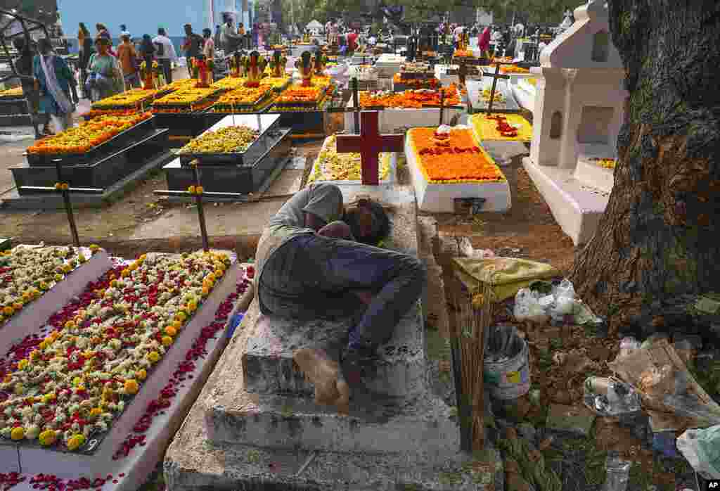 A worker rests on a grave as friends and families gather with candles and flowers to offer prayers for departed souls on All Souls' Day in Hyderabad, India.