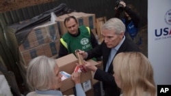 El senador estadounidense Rob Portman, a la derecha, habla con la gente durante una visita a un centro de distribución de la Agencia de Estados Unidos para el Desarrollo Internacional en Kiev, Ucrania, el jueves 3 de noviembre de 2022.