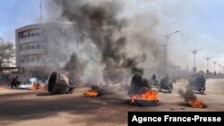 Commuters ride their motorcycles through burning barricades in central in Ouagadougou where group of demonstrators supporting the army protested against President Marc Christian Kabore, in Ouagadougou, Burkina Faso, Jan. 23, 2022.