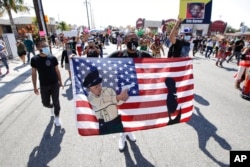 FILE - A protester carries a U.S. flag with added artwork during a march in honor of Andres Guardado in Compton, Calif., June 21, 2020.