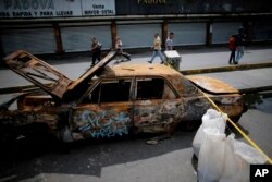 Pedestrians walk past closed shops and a barricade set up by demonstrators on the second day of a 48-hour general strike in protest of government plans to rewrite the constitution, in Caracas, July 27, 2017.