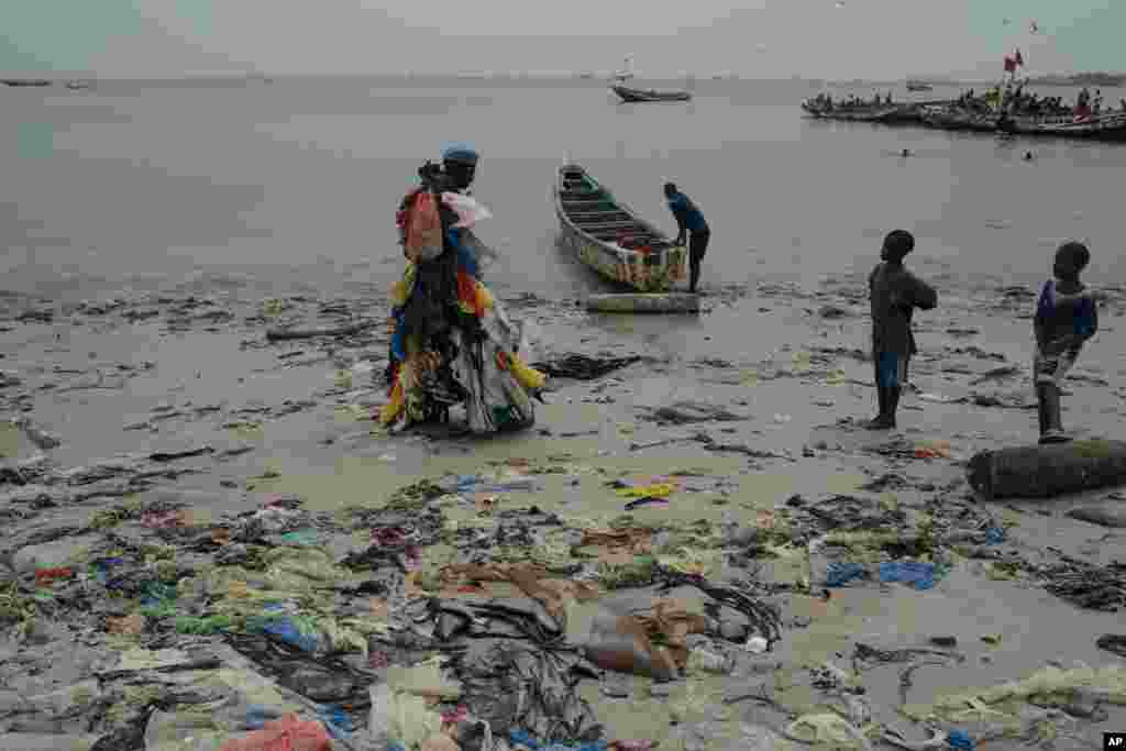 Kids look at environmental activist Modou Fall, who many simply call &quot;Plastic Man&quot;, while he walks on the Yarakh Beach littered by trash and plastics in Dakar, Senegal.